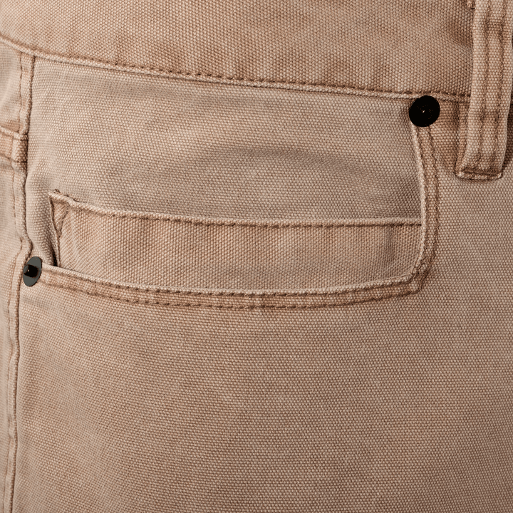 Close-up of tan Badlands pants pocket; metal rivet features the Badlands skull logo for brand identification.