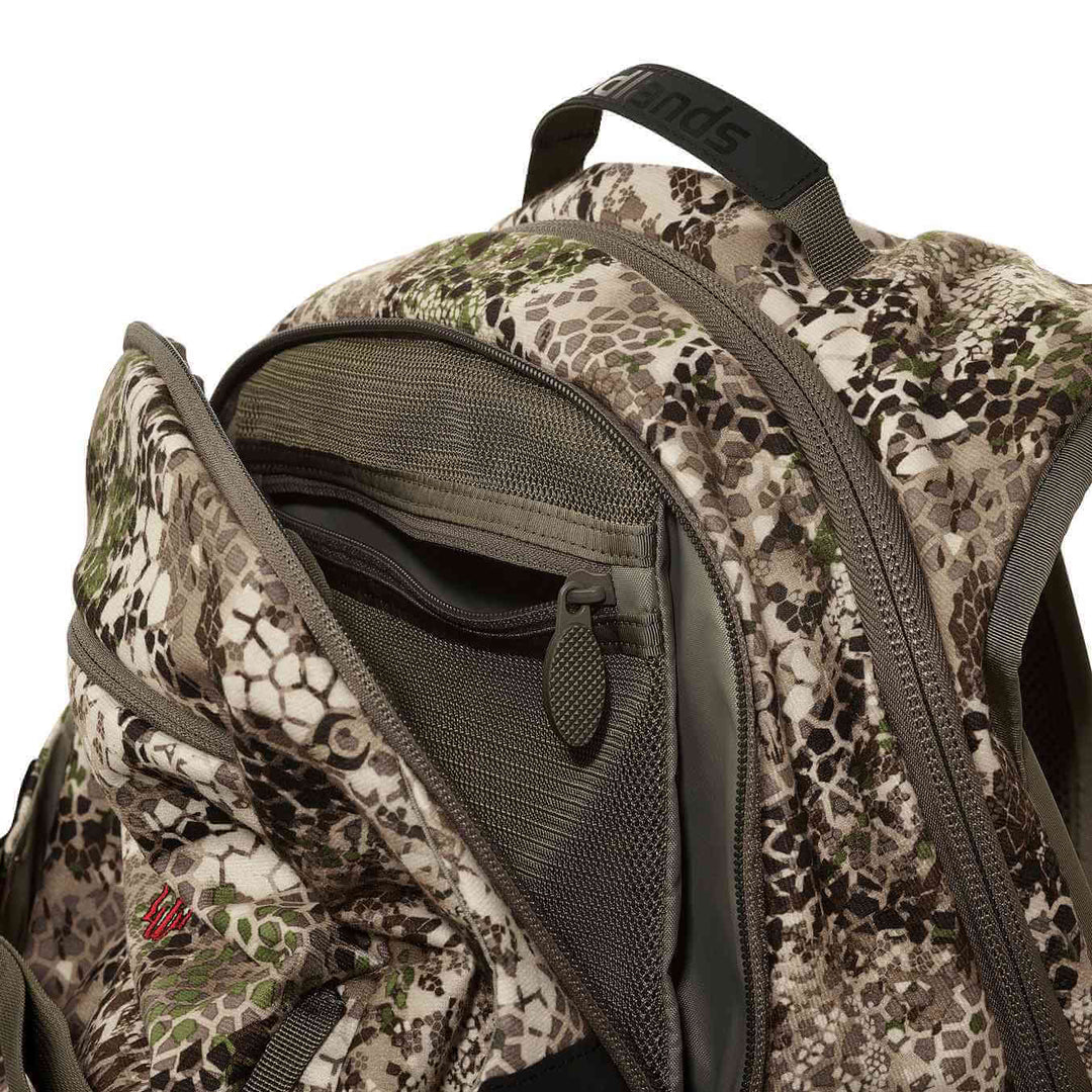Close-up of a Badlands camo backpack, showing open main compartment with mesh pockets and signature skull logo.
