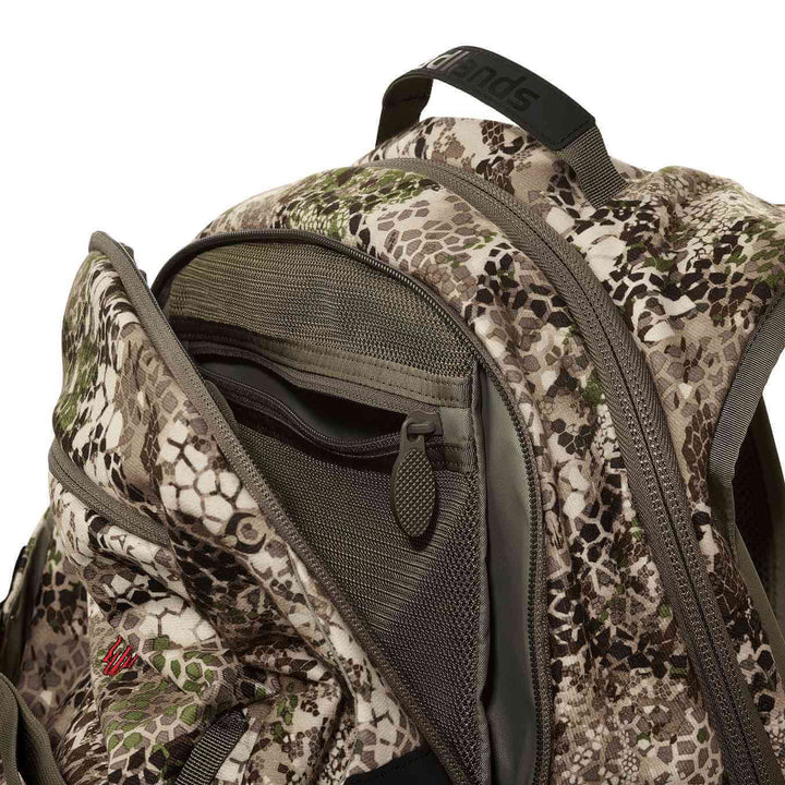 Close-up of a Badlands camo backpack, showing open main compartment with mesh pockets and signature skull logo.