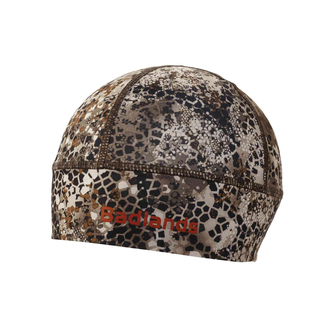 Camo skull cap with Badlands logo in red; lightweight, fitted design for outdoor or hunting use.