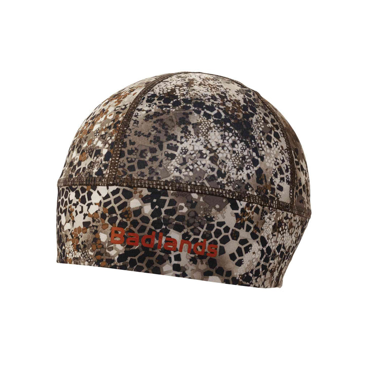 Camo skull cap with Badlands logo in red; lightweight, fitted design for outdoor or hunting use.