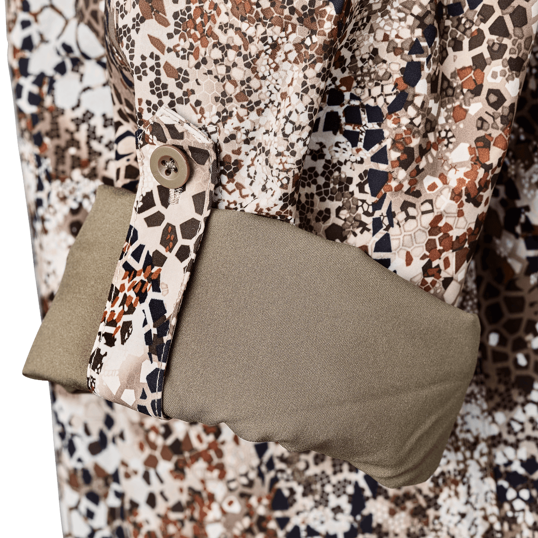 Close-up of a Badlands camo shirt sleeve with button cuff and olive green inner lining, featuring the Badlands skull logo.