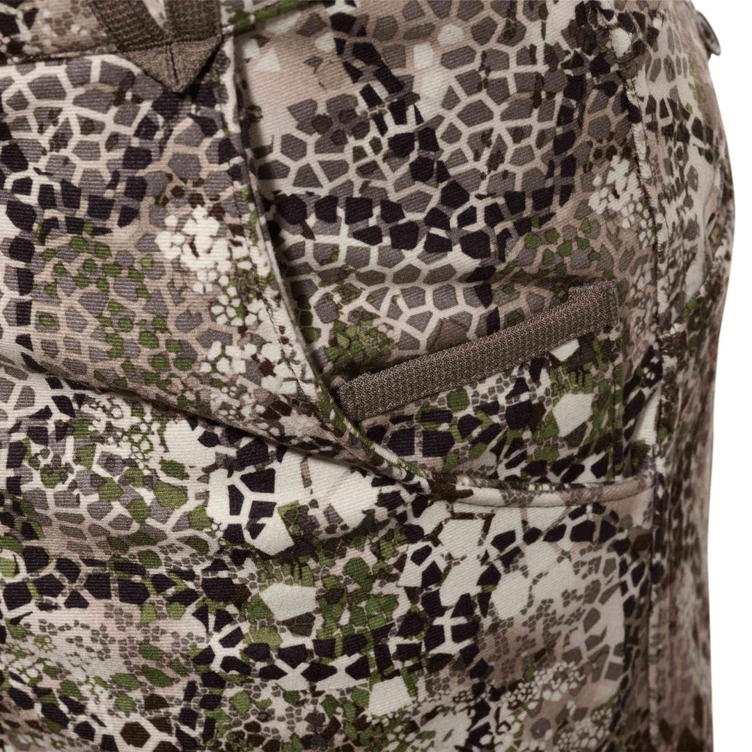 Close-up of Badlands camo fabric with pocket detail; no visible skull logo. Earth tones and geometric pattern.