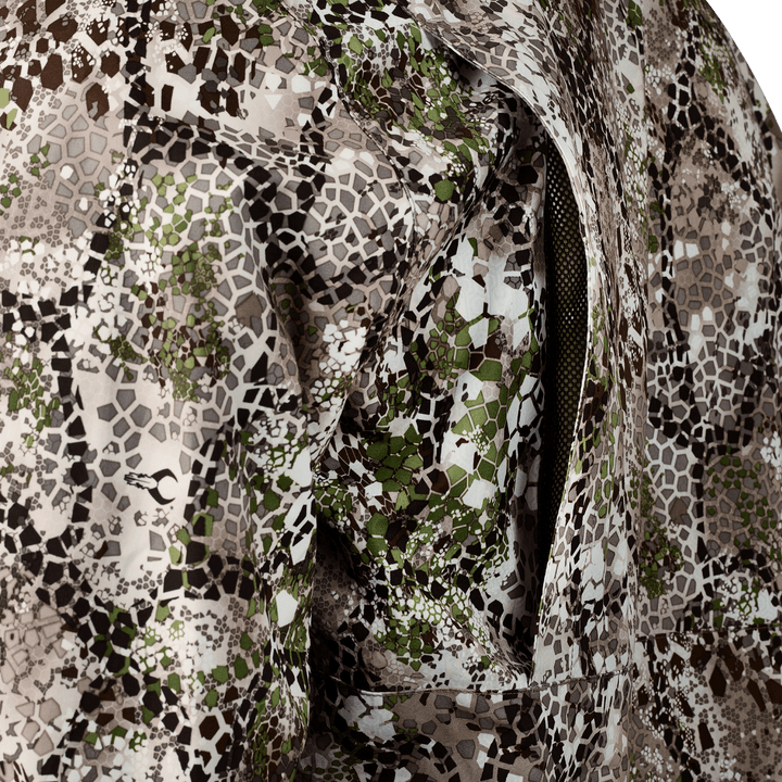 Close-up of Badlands camo fabric with a zippered vent; features hexagonal pattern and subtle Badlands skull logo.